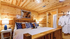 A wooden cabin-style room with a bed, pillows, a clock, and a framed picture on the wall.