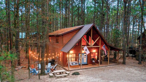 A rustic cabin with a porch, wooden chairs, and a flag.