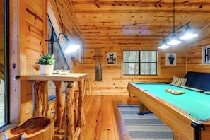 A wooden interior with a pool table, a bar area, and a window with a view.