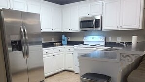 Una cocina moderna con armarios blancos, electrodomésticos de acero inoxidable y piso de baldosas.