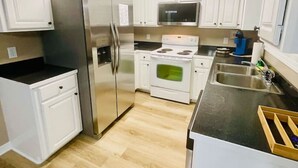 A compact kitchen with white cabinets, stainless steel appliances, and a wooden floor.