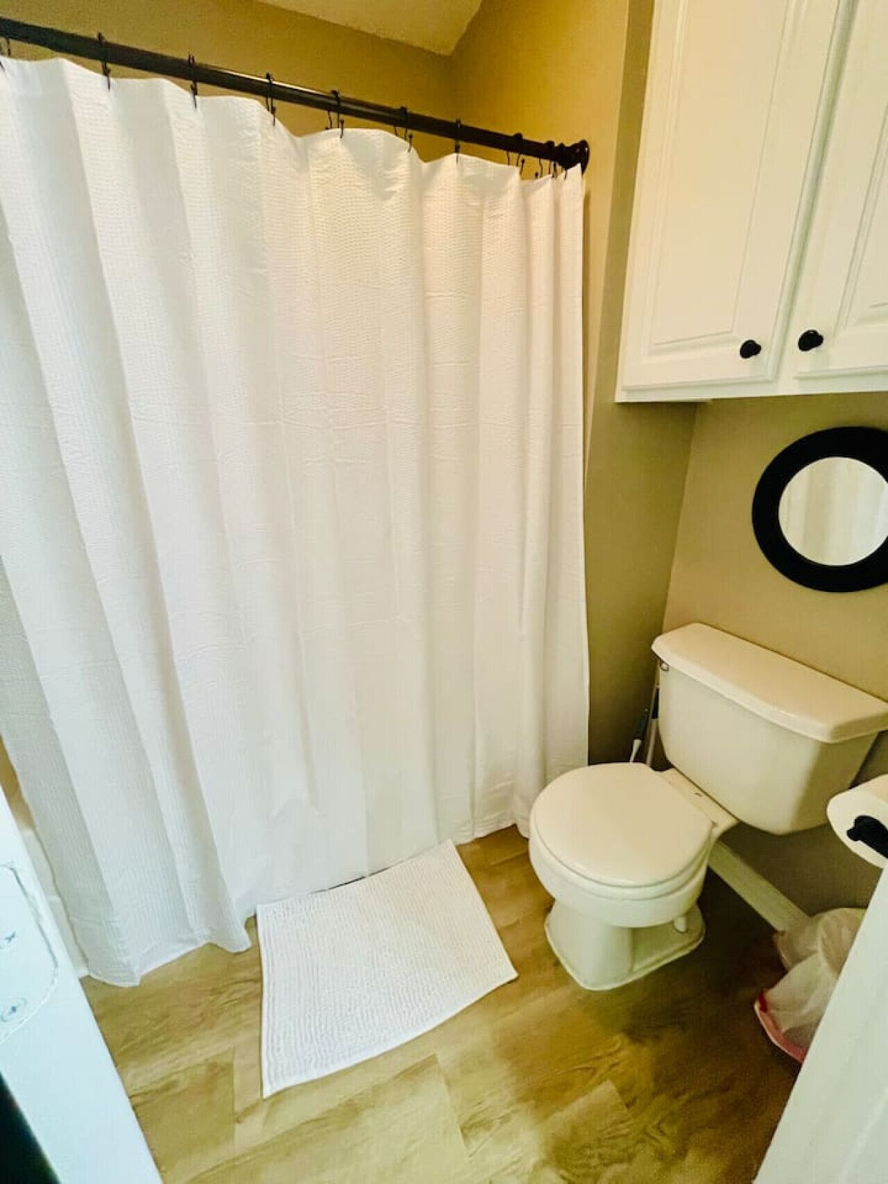 A bathroom with a white shower curtain, a toilet, and a wooden floor.