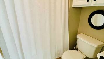 A bathroom with a white shower curtain, a toilet, and a wooden floor.