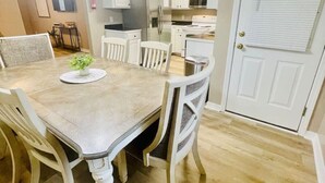 A dining area with a wooden table and white chairs, a kitchen with white cabinets and stainless steel appliances, and a white door with a window.