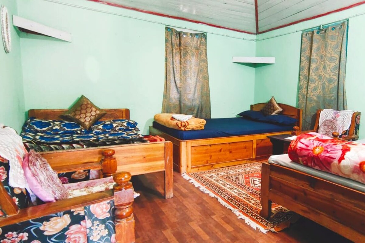 A room with two beds, a wooden chair, a small table, and a patterned rug.