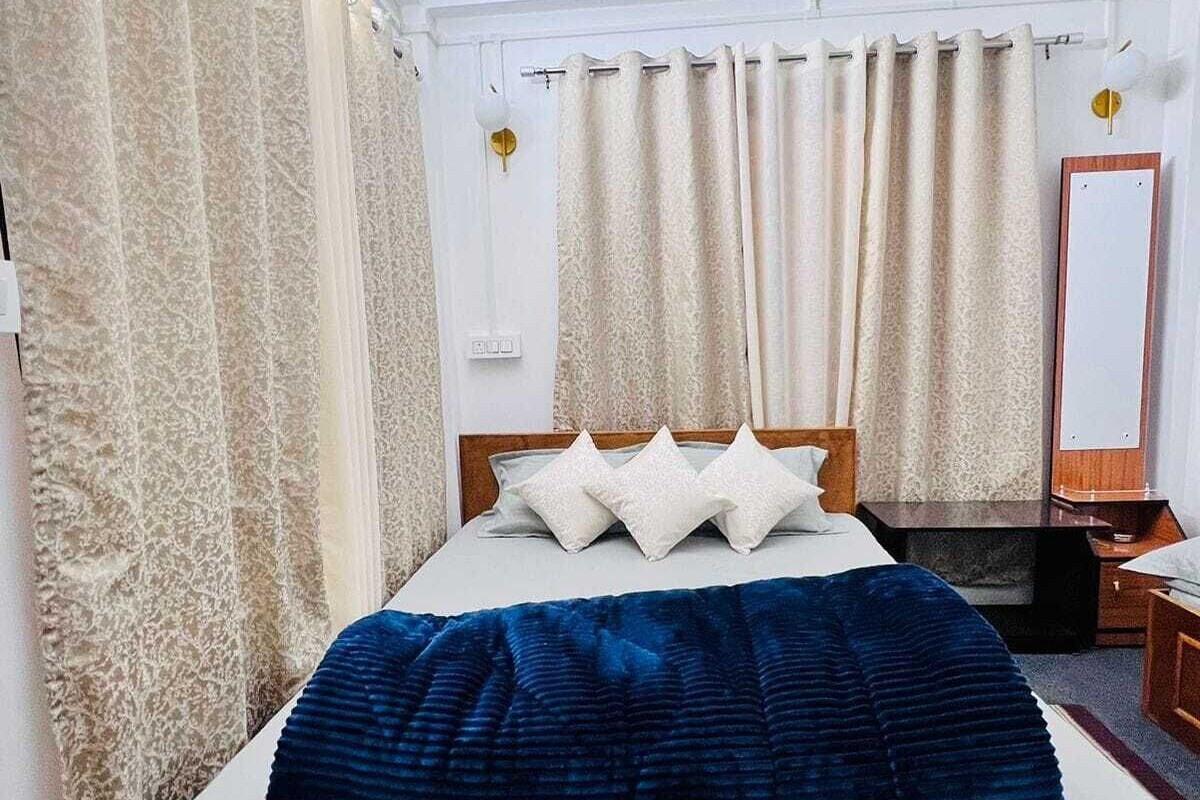 A neatly made bed with a blue blanket, a wooden headboard, and white pillows. There is a wooden nightstand with a lamp and a mirror on the wall.