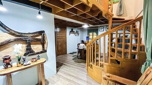Una scala in legno conduce al secondo piano, dove si trova una zona pranzo con tavolo e sedie, e una parete ornata da un'ampia scultura in legno.