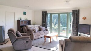 A living room with a sofa, a recliner, a coffee table, a TV, and a sliding glass door to the outside. - Rose End Escape.
Home comfort in the central Wairarapa country side  (Dalefield)