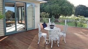 A covered patio with a table and chairs, a potted plant, and a view of a garden and trees. - Rose End Escape.
Home comfort in the central Wairarapa country side  (Dalefield)