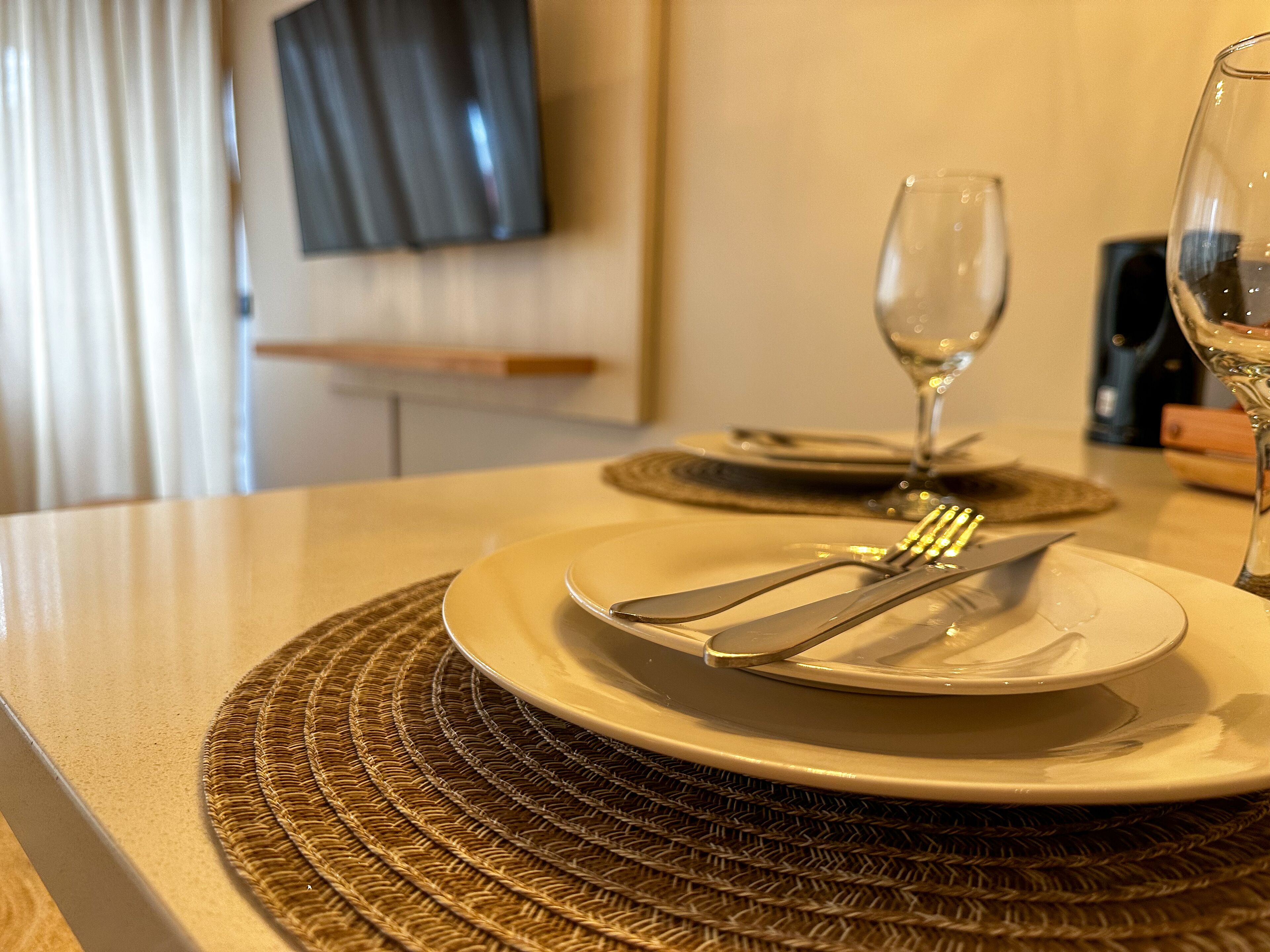 A neatly set dining table with a woven placemat, a wine glass, and cutlery on a plate.