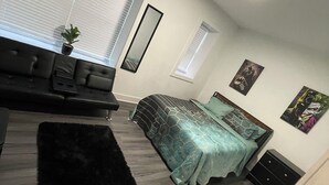 Un dormitorio con cama, sofá, una mesita, espejo y ventana con persianas.
