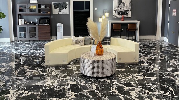 Un vestíbulo moderno con un sofá blanco curvo, una mesa de centro redonda con un jarrón y un suelo de mármol blanco y negro.