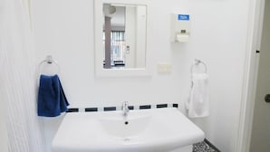 Un baño con un lavabo blanco, un espejo y dos argollas para toallas, una con una toalla azul y otra con una toalla blanca.