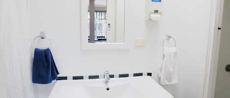 A bathroom with a white sink, a mirror, and two towel rings, one with a blue towel and one with a white towel.