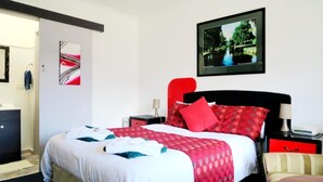 Habitación de hotel con cama, mesita de noche, una silla roja, escritorio y televisor montado en la pared.