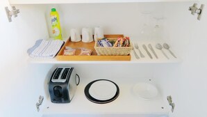 Una encimera de cocina con un tostador, platos, una botella de detergente, una esponja, saleros y pimenteros, una cesta de aperitivos y cubiertos.