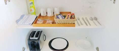 A kitchen counter with a toaster, plates, a bottle of dish soap, a sponge, salt and pepper shakers, a basket of snacks, and cutlery.