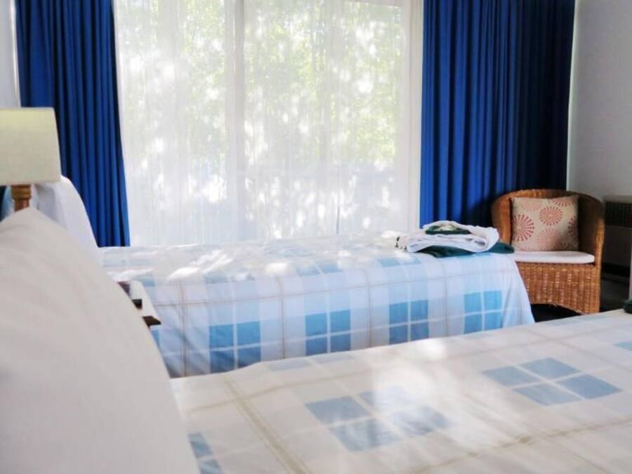 Habitación de hotel con dos camas, una silla, una lámpara y un ventanal con cortinas.