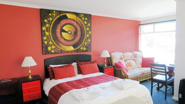 Habitación de hotel con cama, dos mesitas de noche, una silla, un escritorio y un cuadro abstracto grande en la pared.