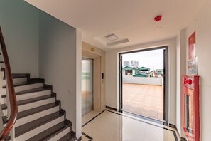 A modern interior with a staircase, an elevator, and a glass door leading to an outdoor area. - Everest Hotel (Hanoi)