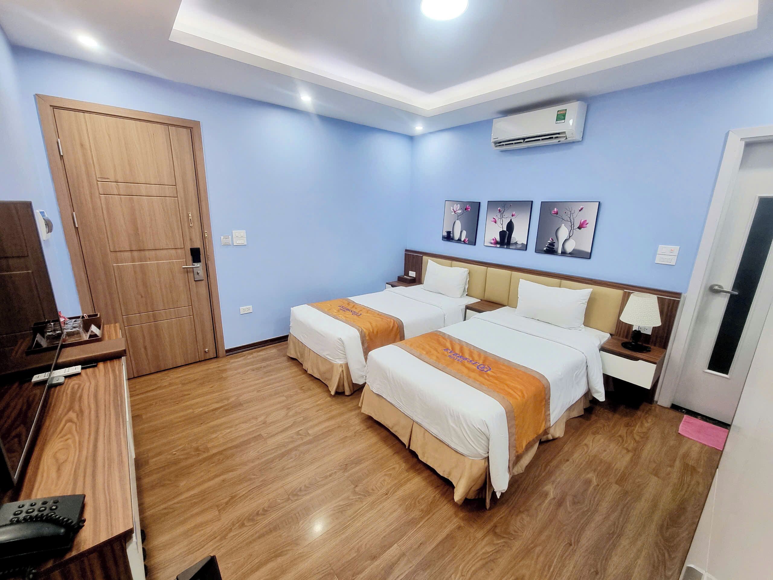 Habitación de hotel con dos camas, un armario de madera, un escritorio con teléfono y aire acondicionado instalado en la pared.