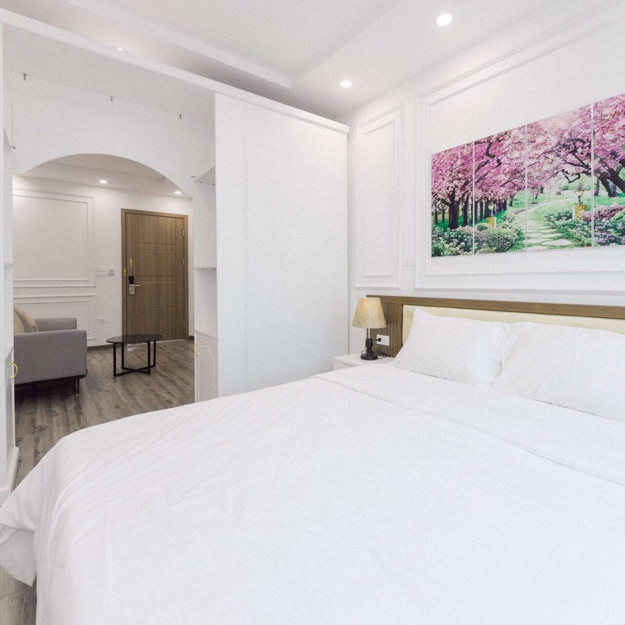 A hotel room with a large bed, a desk, a chair, a lamp, and a painting of a garden.