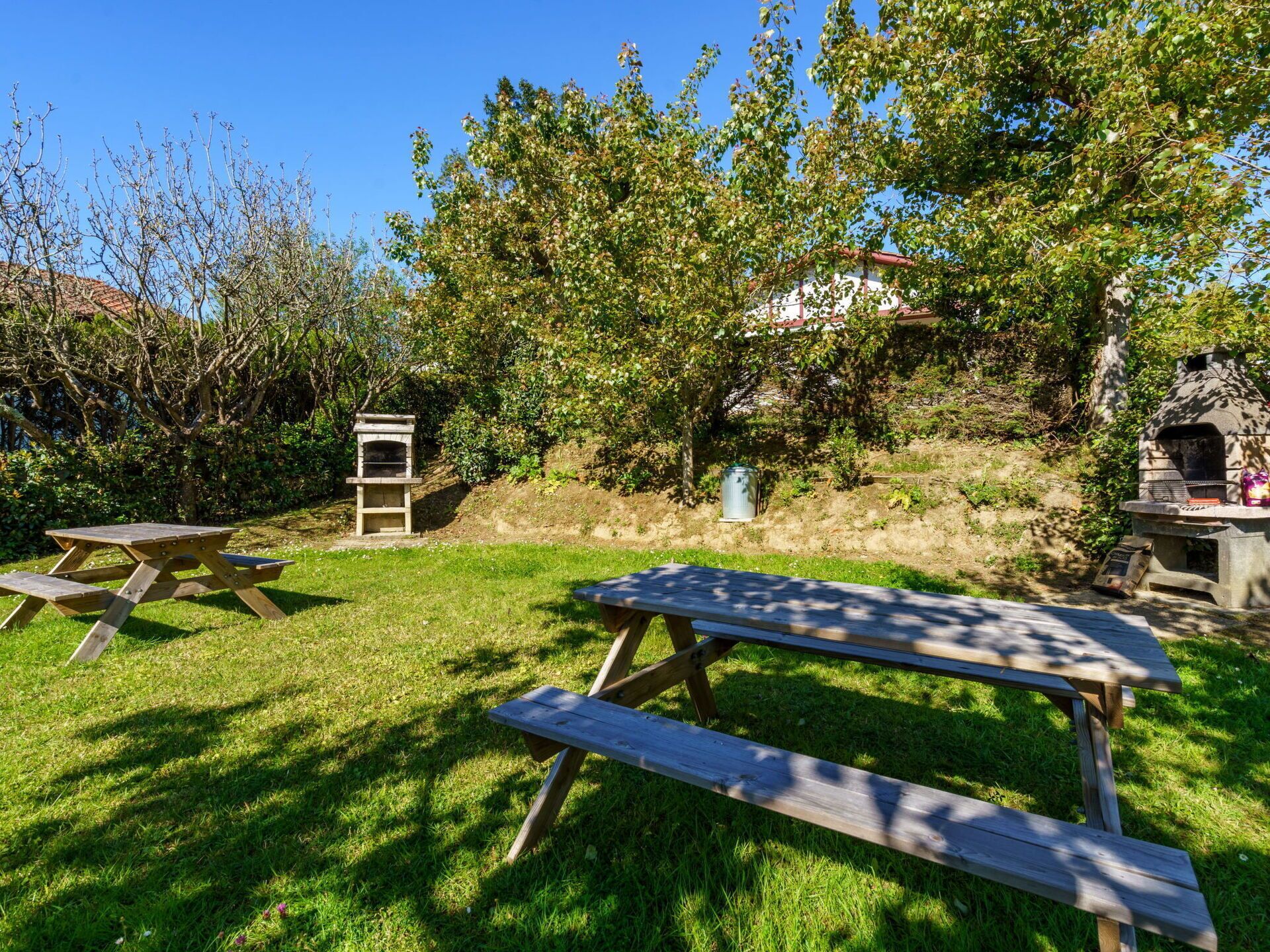 A backyard with picnic tables, a barbecue grill, and a stone oven.