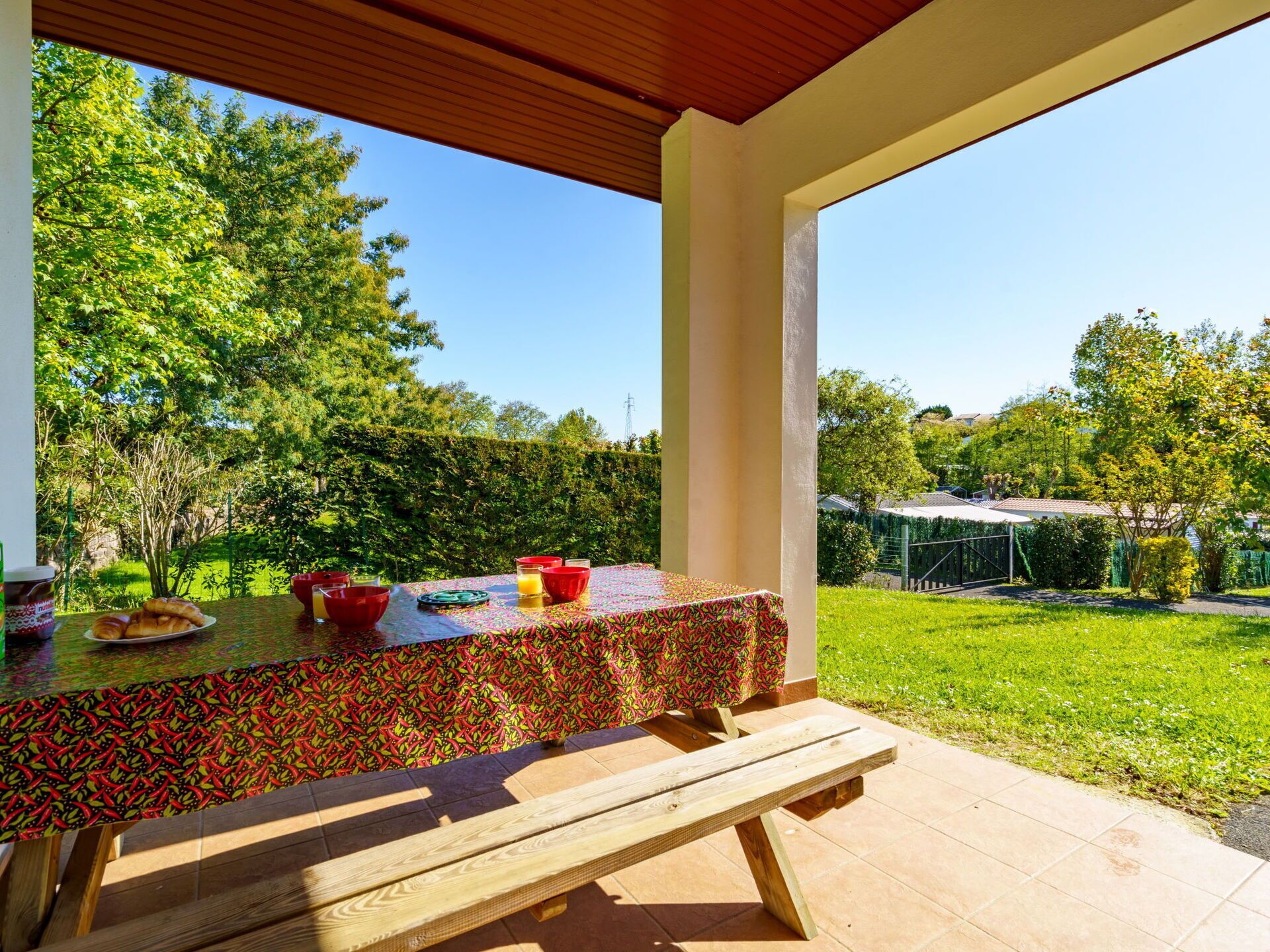 An outdoor patio with a table set for breakfast, surrounded by a lush garden and a clear sky.