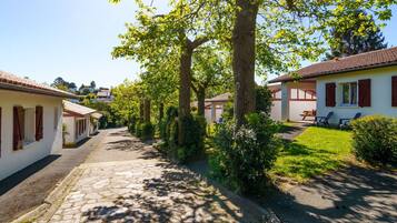 Een smalle straat met keien, omzoomd door witte gebouwen met rode luiken, die leidt naar een overdekt terras met buitenplaatsen.