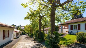 A narrow cobblestone street lined with white buildings with red shutters, leading to a covered patio area with outdoor seating. - Lovely apartment in villa for 6 people with WIFI, pool, TV and terrace (Guéthary)