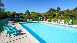 A rectangular swimming pool with a tiled deck, surrounded by white lounge chairs and a green fence. - Lovely apartment in villa for 6 people with WIFI, pool, TV and terrace (Guéthary)