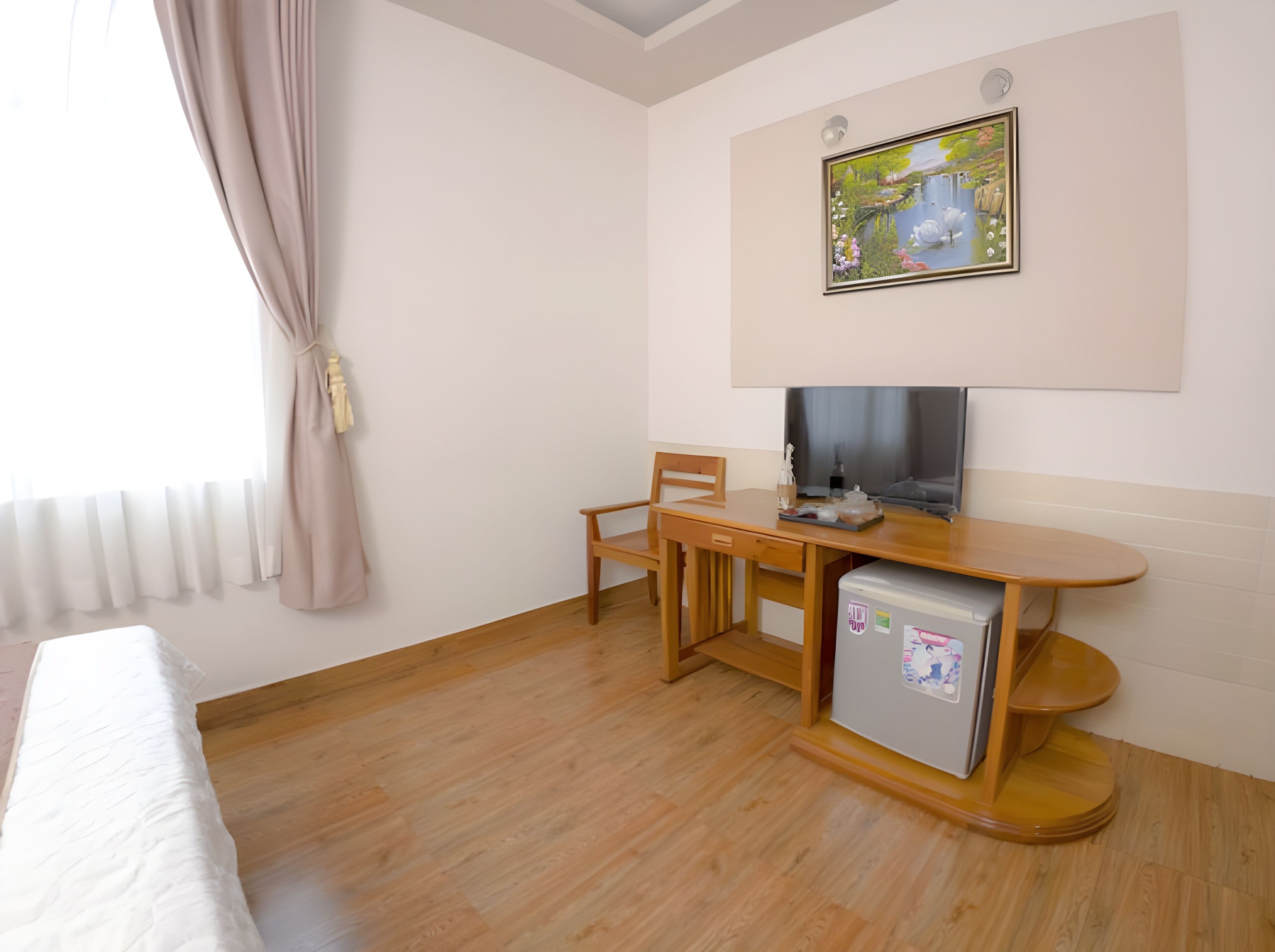 A hotel room with a bed, a wooden desk, a television, and a small refrigerator.