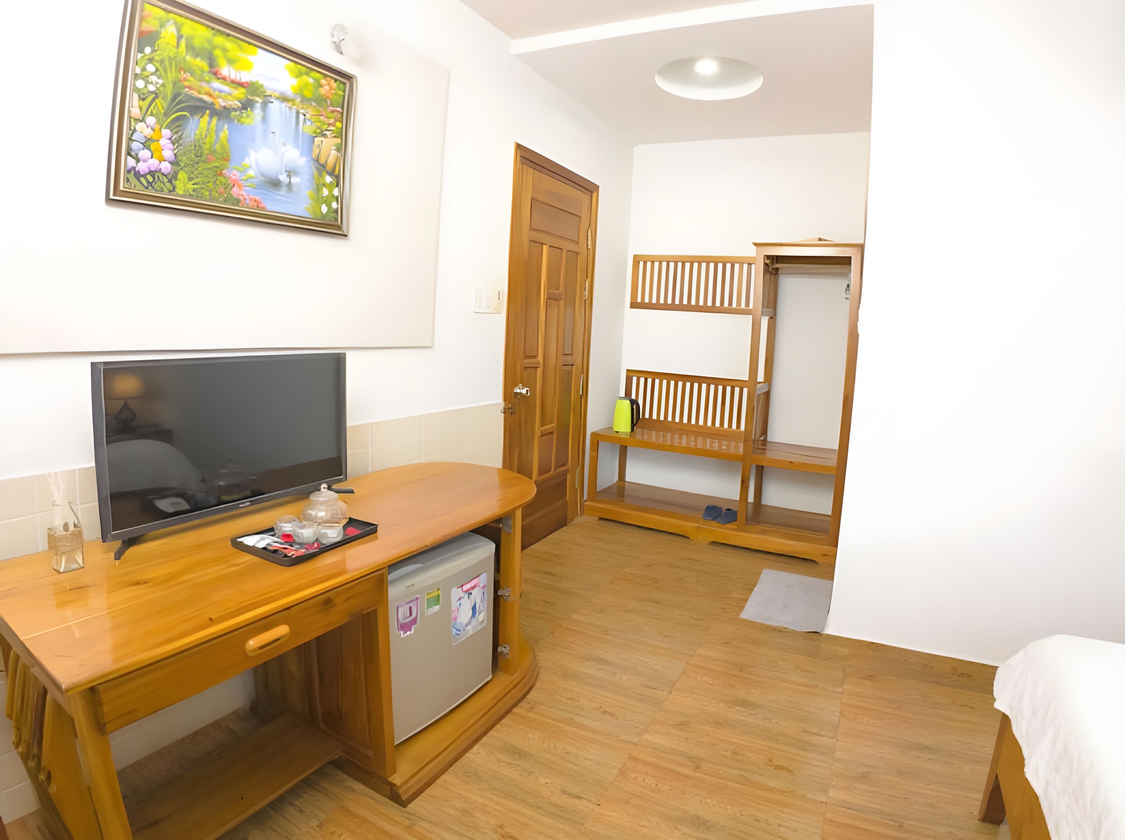 Une chambre de taille modeste, comprenant un bureau en bois, une télévision, un petit réfrigérateur, une armoire en bois et un lit.