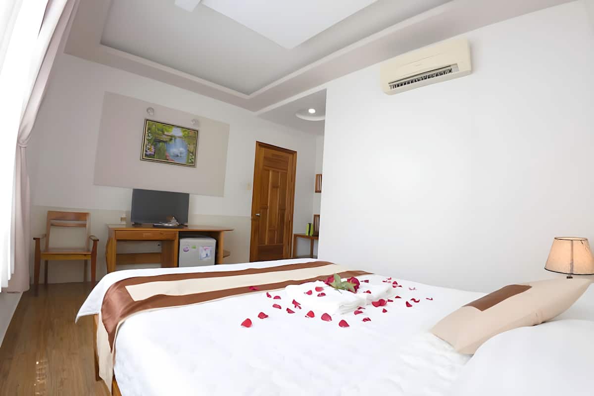 A hotel room with a bed, a desk, a television, and a door.
