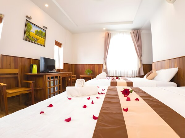 A hotel room with two beds, a desk with a television, wooden paneling, and a painting on the wall.