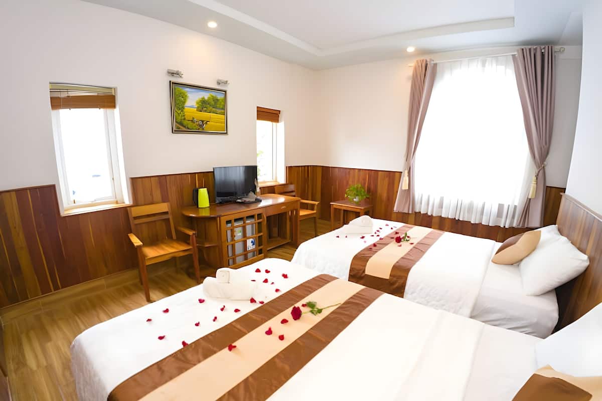 A hotel room with two beds, a desk with a computer, a TV, and a window with curtains.
