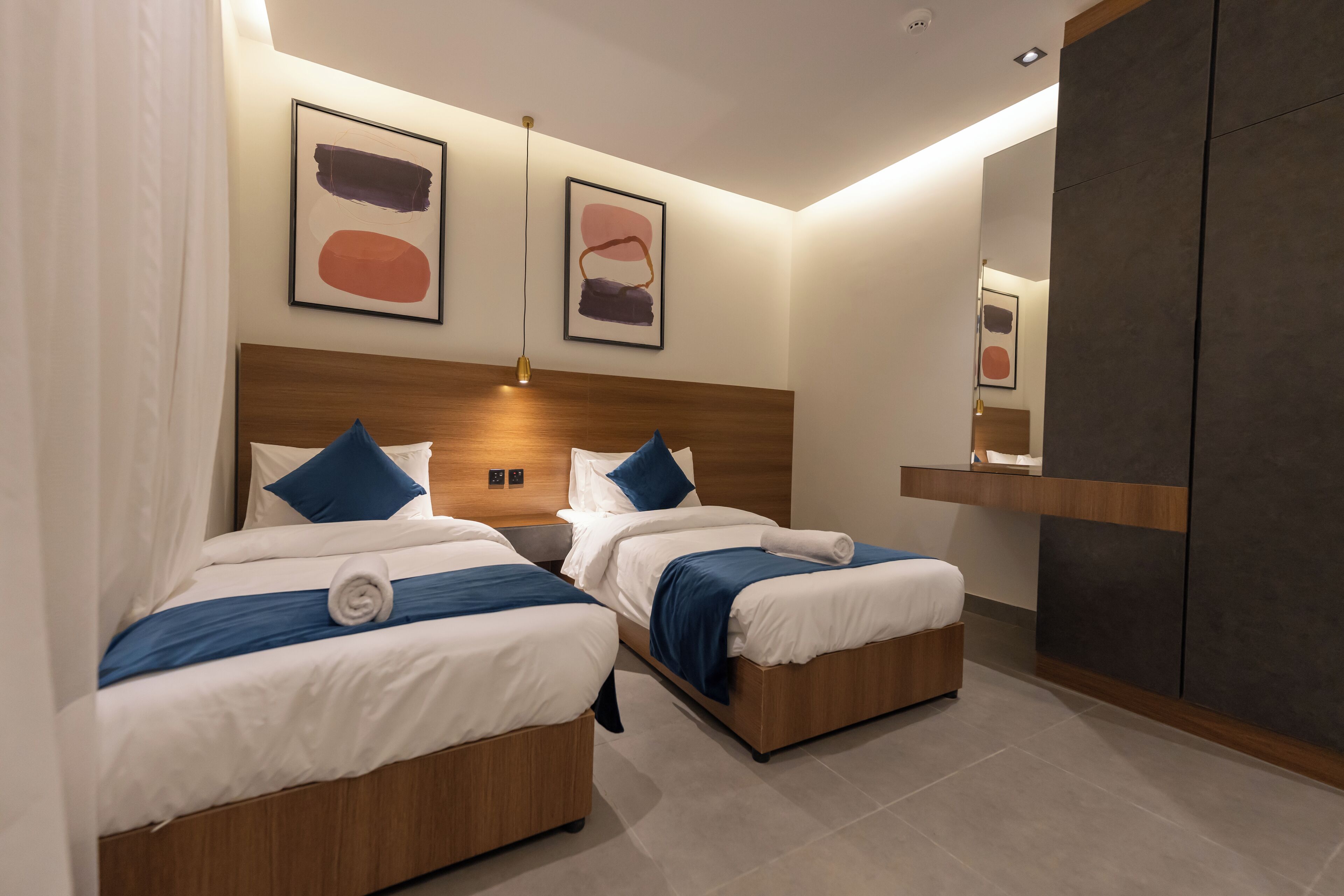 A modern hotel room with two single beds, a wooden headboard, and a large mirror.