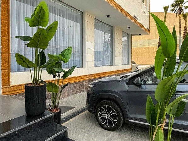 Un edificio moderno con ventanas amplias, un automóvil estacionado adelante y plantas en macetas.