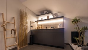 A modern kitchen with a dark countertop, wooden ladder, decorative plants, and a built-in shelf with kitchenware. - Arjaan Park Al Shifa (Riyadh)
