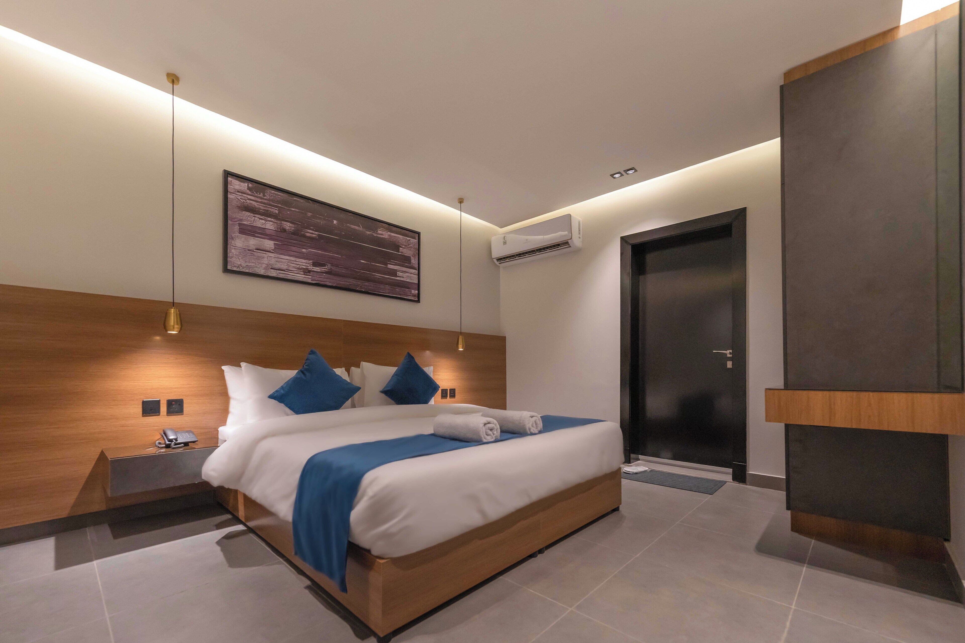 A modern hotel room with a large bed, bedside tables, a wall-mounted air conditioner, and a door.