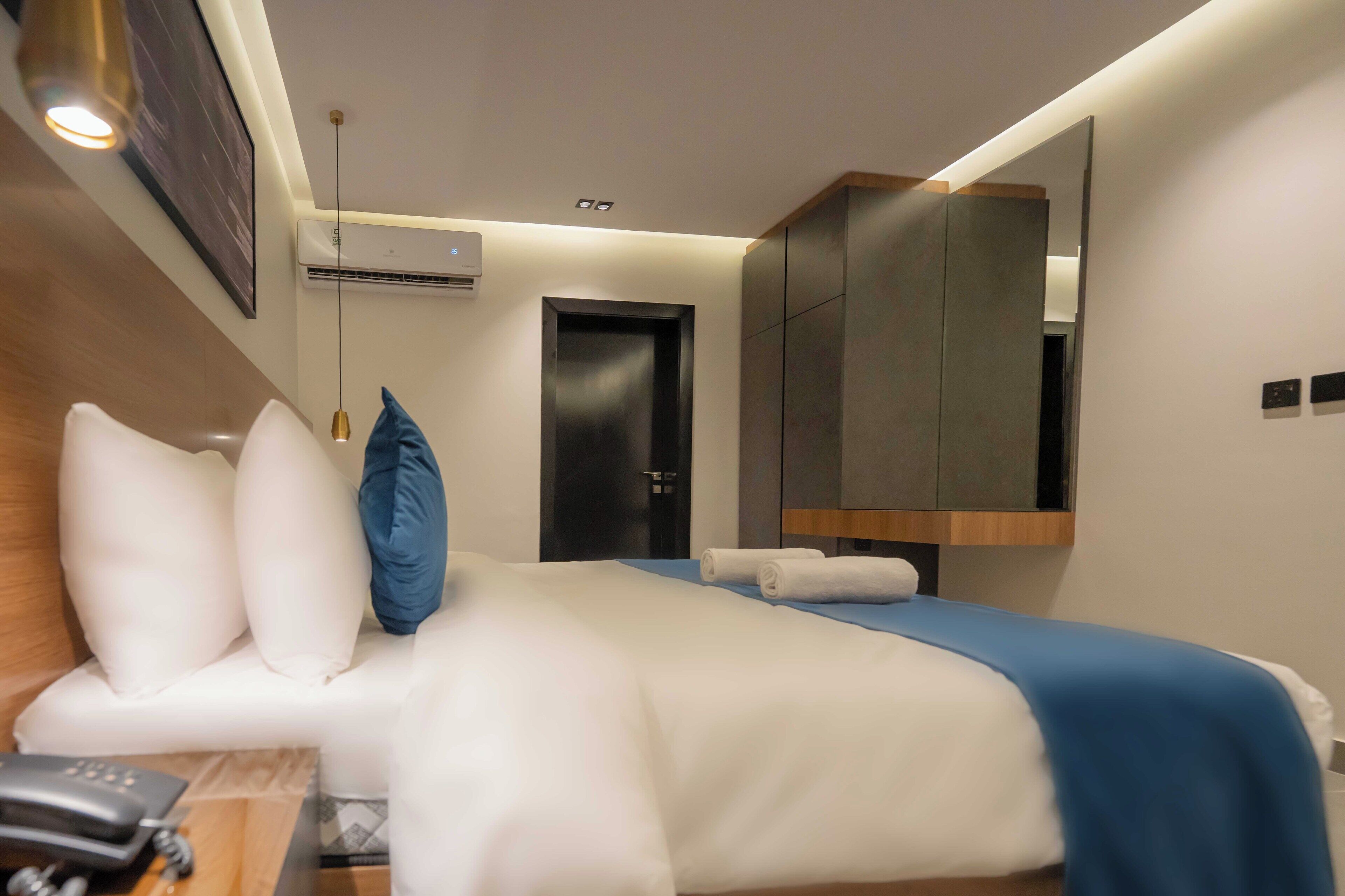 Une chambre d’hôtel comprenant un lit, un bureau avec un téléphone, un climatiseur fixé au mur et une porte.