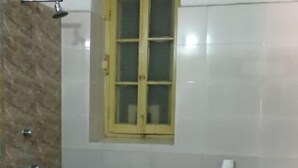 A bathroom with a toilet, a shower, a window, and a red bucket. - YWCA GALLWAY GUEST HOUSE (Kolkata)