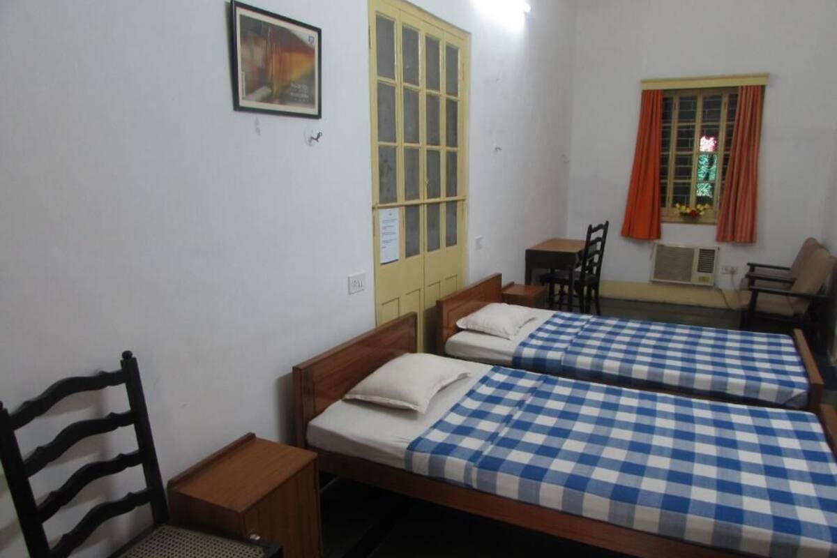 A room with two beds, a wooden chair, a small table, and a window with curtains.