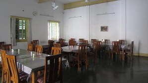 A conference room with multiple tables and chairs, ceiling fans, and windows with curtains. - YWCA GALLWAY GUEST HOUSE (Kolkata)