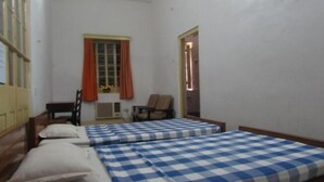 A room with two beds, a chair, a small table, and a window with curtains. - YWCA GALLWAY GUEST HOUSE (Kolkata)