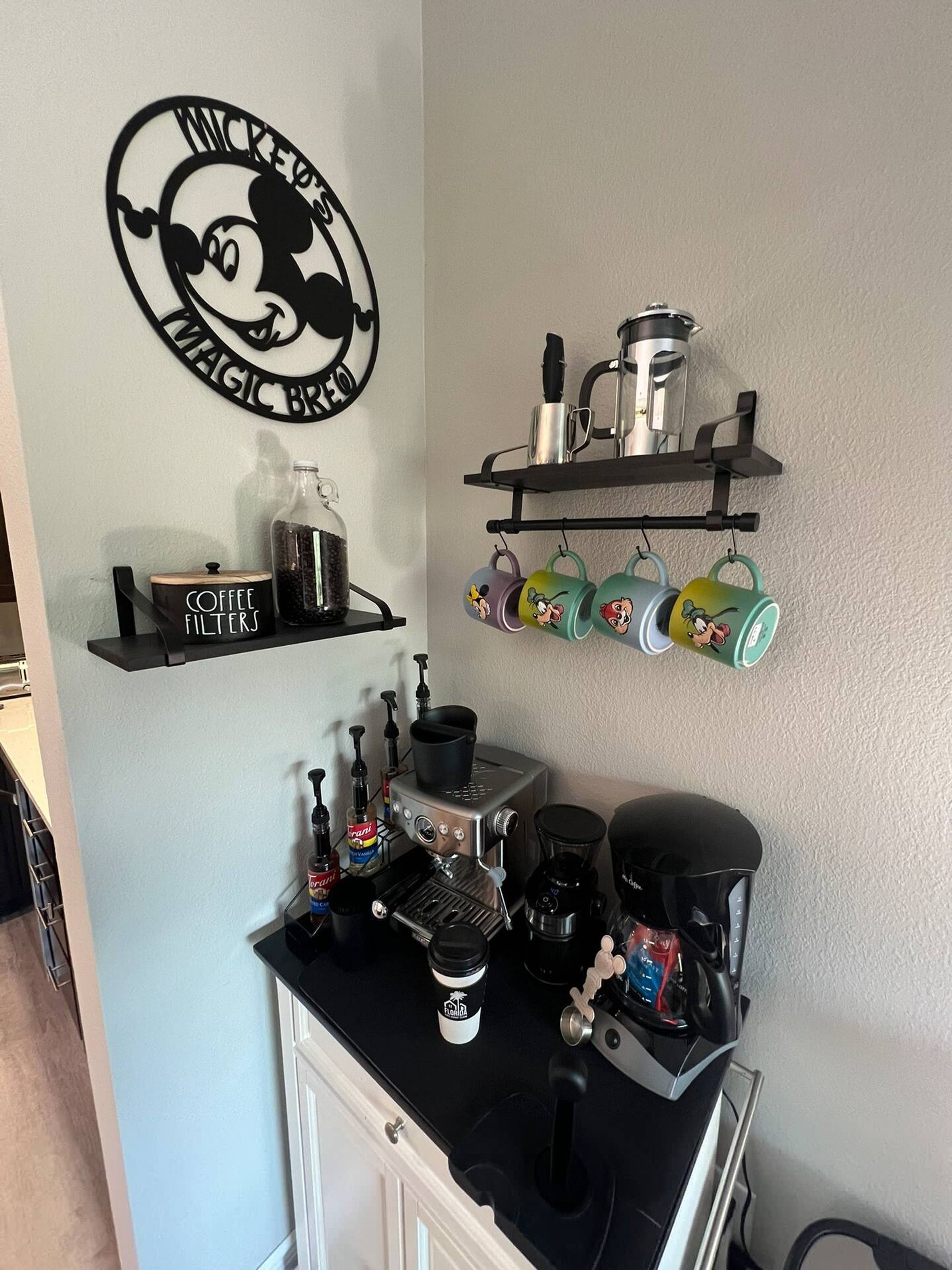 Een aanrecht met koffiezetapparatuur, een koffiefilterhouder en een muurdecoratie met Mickey Mouse.