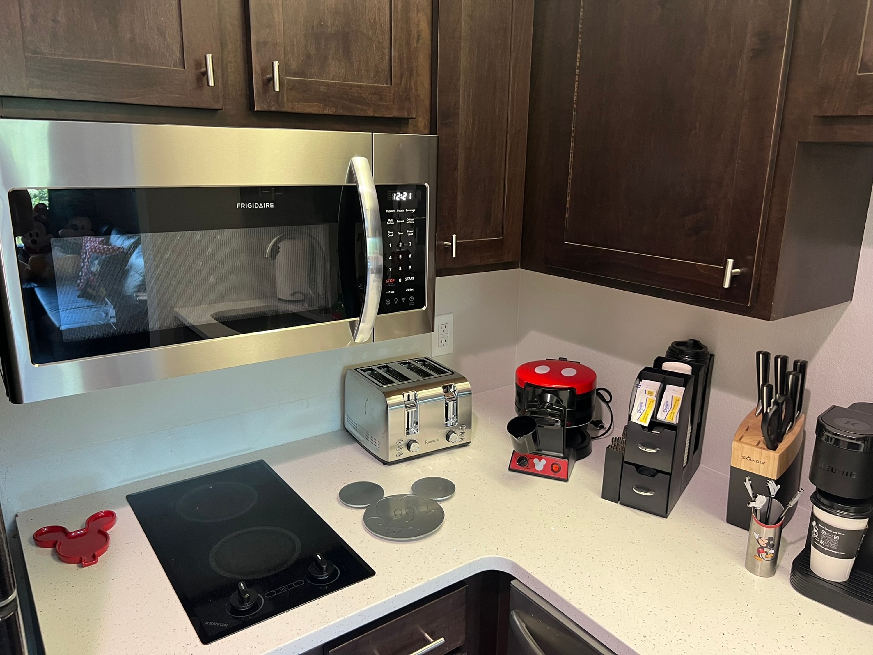 Une cuisine équipée d’un four à micro-ondes, d’un grille-pain et d’une machine à café en acier inoxydable, ainsi que d’une plaque de cuisson à induction décorée aux couleurs de Mickey Mouse.