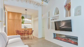 Een moderne woonkamer met een witte bank, eettafel, stoelen en een aan de muur bevestigde televisie.