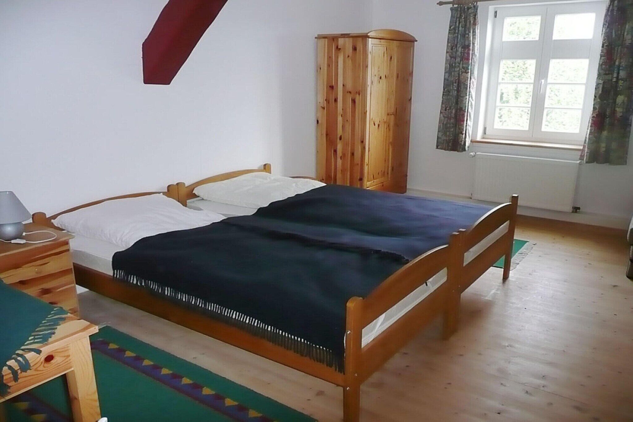 Un dormitorio con cama de madera, un armario, una ventana con cortinas y una mesita de noche con lámpara.