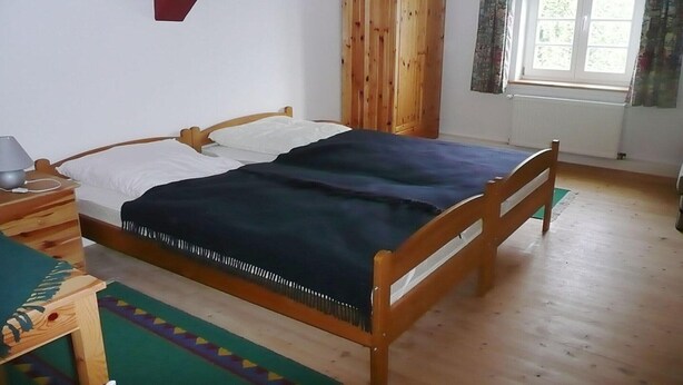 A bedroom with a wooden bed, a wardrobe, a window with curtains, and a bedside table with a lamp. - Ferienwohnung Kemenate (Trendelburg OT Wülmersen)